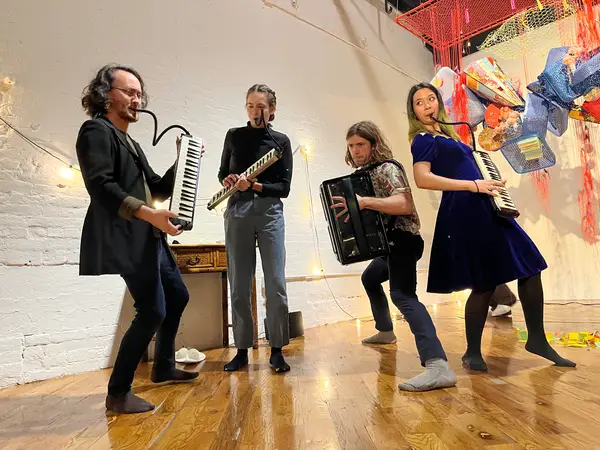 The ensemble holding their instruments (three melodicas and one accordion) and making silly faces